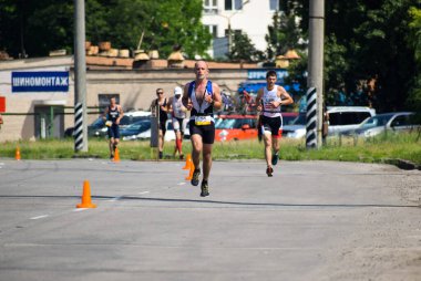 POLTAVA, UKRAINE - 19 Haziran 2021: Triatlon yarışmaları sırasında yaz öğleden sonra koşucular yolda koşar