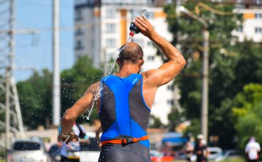 POLTAVA, UKRAINE - 19 Haziran 2021: Bir adam triatlon yarışması sırasında yaz öğleden sonra koşarken su döker