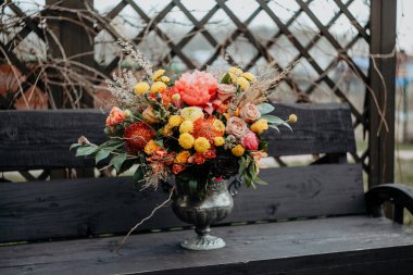 Sulu, parlak bir sonbahar buketi, boho stili düğün buketi, buketin kompozisyonu kırmızı turuncu çiçekler, bahçede bir buket çiçek duruyor.