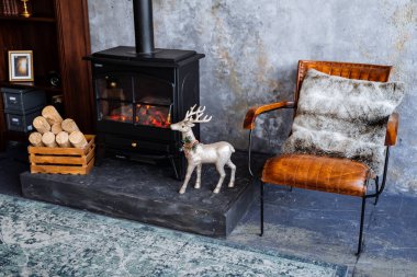 Oturma odasında şömine, apartmanın içinde yeni yıl, yanan şöminenin yanında bir sandalye oyuncaklarla süslenmiş bir Noel ağacı, ağacın altında hediyeler, iç dizayn.