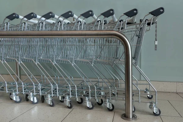 Metal shopping carts pushed into each other in a row - side view in a hallway with a metal bar as separation