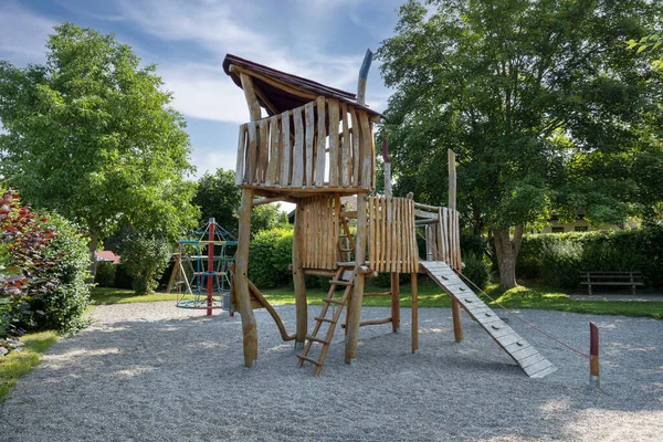 Çocuk parkında ağaçtan yapılmış bir oyun evi. Sonbahar koruması altında. Küçük gölgeli bir parkta büyük ağaçları olan çakıllar.