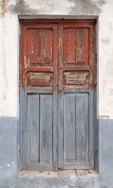 Old, heavily weathered, gray red door made of wood, detail in a run-down facade