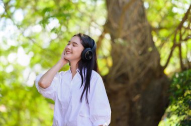 Genç, gülümseyen bir kadın, dinleniyor ve kulaklıkla müzik dinliyor.