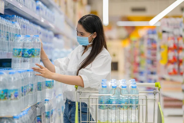 Süpermarketten yüz maskesi takan bir kadın. Coronavirus covid-19 pandemisi sırasında panik alışverişi. Malzeme dükkanından bütçe alımı..