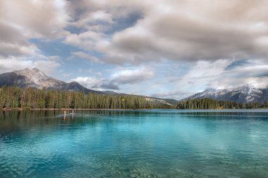 Maligne Gölü, Jasper Alberta Kanada Ulusal Parkı 'nda güzel turkuaz göl ve kristal berrak mavi gökyüzü ve arka planda bir çam ormanı ve dağları olan kızıl bulutlar..