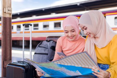 İki Müslüman kadın haritaya baktı ve platformda treni beklerken mutlu bir şekilde gülümsedi..