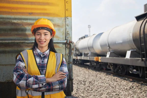 Portrait of female engineer standing and arms crossed outdoors and petroleum tanker train. The petroleum transportation industry by a rail system.