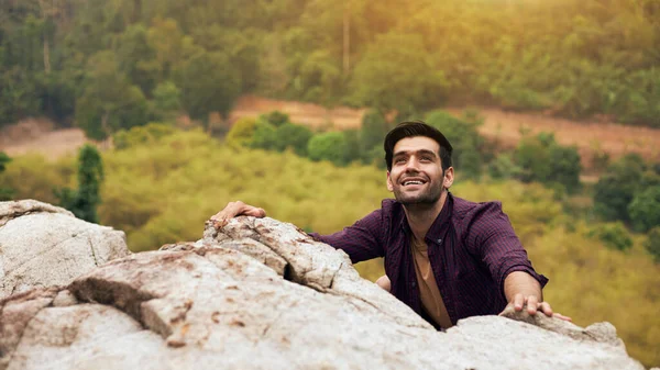 A handsome caucasian man is trying to climb a rock to the top of the mountain during vacation trips. Concept of trying to focus on goals and success.