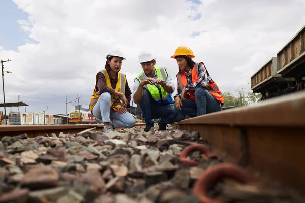 Successful Rail logistics specialists or train engineers wearing helmets and safety vests are conducting inspections and meeting a work plan for managing a freight train on the train tracks.
