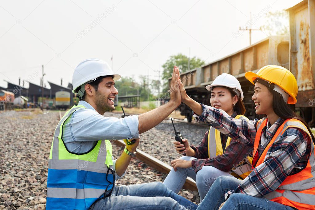 Three train engineers wearing helmets and safety vests were chatting or meeting happily on an outdoor track during the day. Successful Rail logistics specialist setting up a transport system.