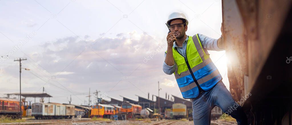 Successful Rail logistics specialists or train engineers wearing helmets and safety vests standing outdoors on the train holds a walkie-talkie checking the readiness of work.