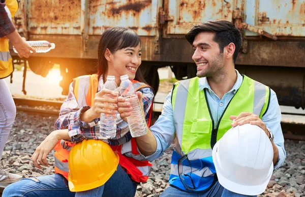 Industrial workers or Rail transport engineers in protective clothing are drinking water to quench their thirst beside the freight train after working hard during the day outdoors.