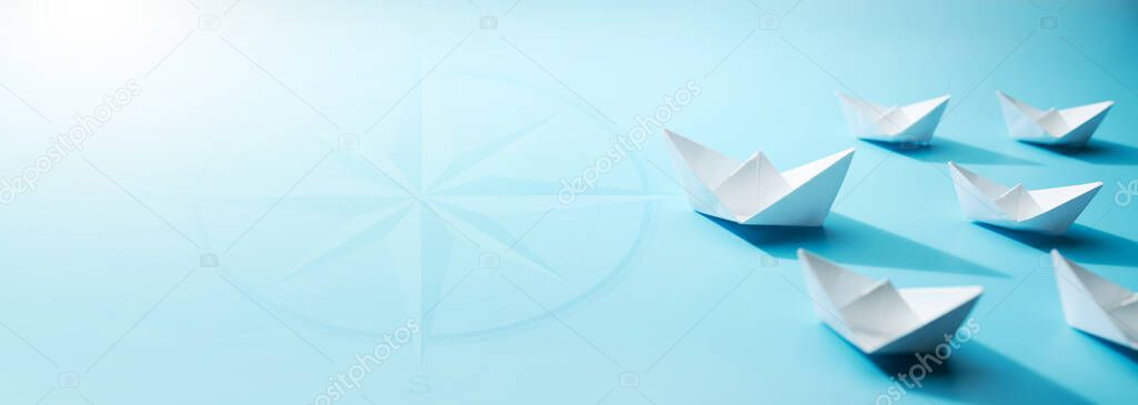 A fleet of small white paper boats on the blue background was headed towards the light at the horizon. Concept of leading the organization towards its goals.