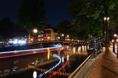 Amsterdam 'da bir gece. Kanaldan aşağı süzülen bir teknenin ışık çizgileri. Yaz.