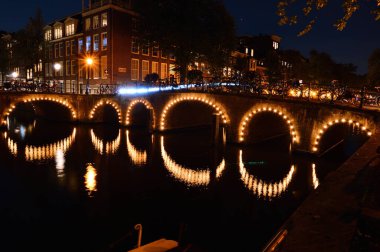 Amsterdam 'da bir gece. Aydınlatılmış köprü kanal suyuna yansıyor. Yaz.