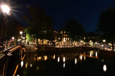 Amsterdam 'da bir gece. Aydınlatılmış köprü kanal suyuna yansıyor. Yaz.
