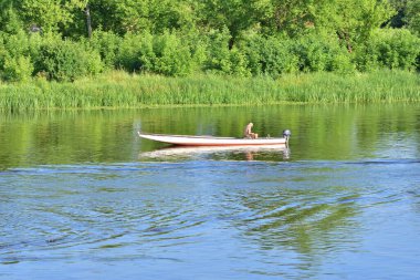 Bir balıkçı teknede nehirde balık tutuyor. Yaz.