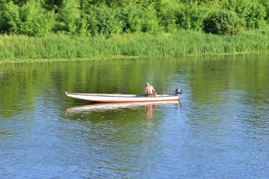 Bir balıkçı teknede nehirde balık tutuyor. Yaz.