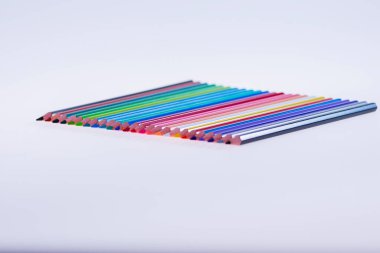 Beyaz arka planda 24 renkli boya kalemi, düzgün düzenlenmiş ve sivriltilmiş. Merhaba okul.