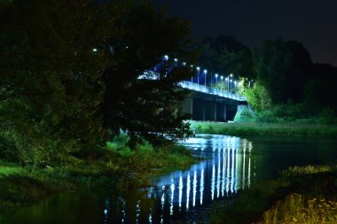 Köprü, alacakaranlıkta ağaçlar arasında LED fenerlerle aydınlatıldı. Nehir.