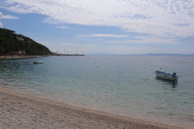 Şeffaf bir denizde deniz manzaralı bir körfez ve güneşli bir yaz gününde sirrus bulutlu mavi bir gökyüzü. Temiz turkuaz suyu olan güzel bir koyda çakıl taşı plajı, sakin bir deniz ve gökyüzünün zemininde kayıklar, Hırvatistan