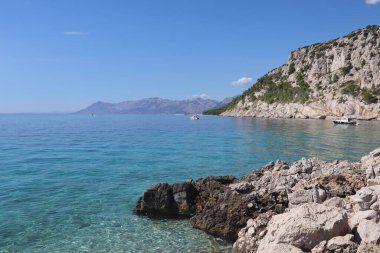 Güneşli bir yaz gününde, Adriyatik Denizi 'nin turkuaz ve kayalıkların manzarası. Kayalık bir sahilde deniz manzarası, şeffaf gök mavisi deniz, parlak mavi bir gökyüzüne karşı tekne, Hırvat kıyısı.