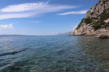 Hırvatistan kıyısında güzel bir körfezin manzarası. Açık deniz ve dağ yamaçları, bulutlu açık mavi gökyüzünün arka planına karşı. Adriyatik Denizi 'nin şeffaf turkuaz suyu, kayalık kıyı şeridi, güneşli bir yaz gününde Hırvatistan kıyıları.