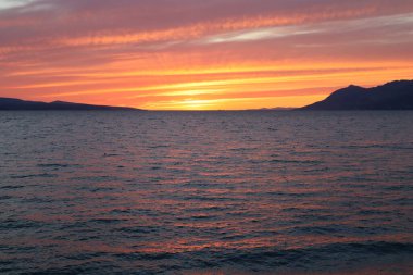 Adriyatik kıyılarında parlak kırmızı turuncu gün batımı, parlak bulutlar ve güneş ışınları deniz yüzeyine yansıyor