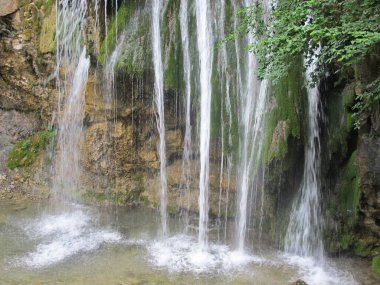 Dağlık Kırım 'da güzel bir şelale ıslak kayaların ve yeşil yosunların arka planında su fışkırıyor. Şelalenin manzarası Dzhur-Dzhur dağ nehri kayanın yüksek bir çıkıntısından dökülüyor 