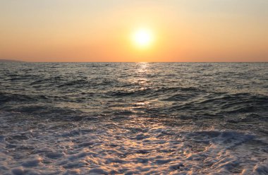 Yaz denizinde akşamları sarı-turuncu tonlarda gün batımı. Resimli akşam denizi ve turuncu gökyüzü ve gün batımında parlak güneş.