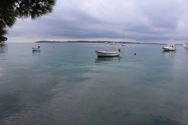 Calm at sea before rain, stormy gray clouds in the sky, boats on the surface of calm water. Seascape of an anchored boat and stormy sky before rain on the Croatian sea coast