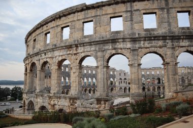 Pula 'daki oliseum manzarası, arena ve taş duvarlar antik Roma amfi tiyatrosunun kemerleriyle Hırvatistan' da bir sonbahar günü gri-mavi gökyüzü ve denizin arka planına karşı,