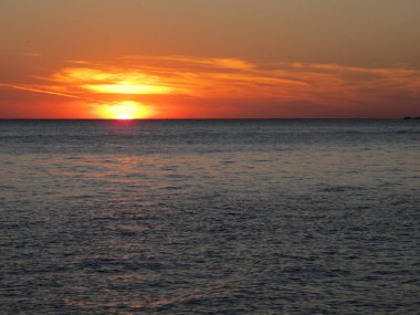 Sahilde Parlak Gün Batımı. Deniz manzarası ufukta batıyor su yüzeyinde, sarı-turuncu bulutlar ve gökyüzü