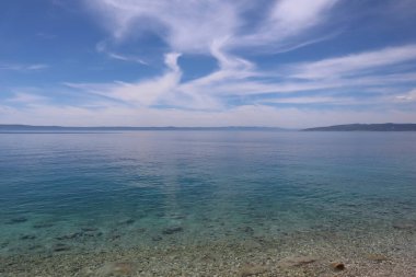 Hırvatistan 'ın yazlık güneşli bir gününde, turkuaz deniz üzerinde mavi gökyüzünde beyaz deniz manzaralı bulutlar. Deniz suyunun şeffaf olduğu plaj ve mavi gökyüzünde kalp şeklinde bulutlar.