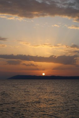 Denizde parlak gün batımı, turuncu gökyüzü ve denizin üzerinde güneş ışığı.