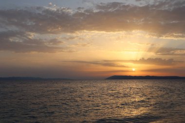 Deniz üzerinde parlak turuncu gün batımı, güzel bulutlar ve güneş ışınlarıyla gökyüzü.