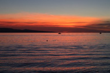 Deniz üzerinde deniz gün batımı, parlak kırmızı gökyüzü, ufukta bulutların ardında güneş.