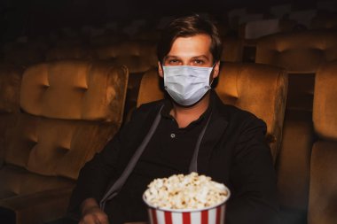 Sinemadaki sosyal mesafeler: Yabancı erkek tüketiciler Coronavirus 'un (Covid-19) yemek için patlamış mısır tutmasını önlemek ve güvenlik önlemlerine göre aralıklarla oturmasını önlemek için sinemalarda maske takıyorlar.