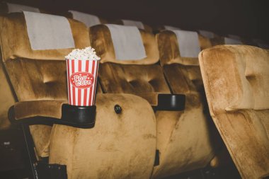 Patlamış mısır kırmızı kağıt bardakta paketlenir. Bir sinema salonundaki sandalyeye yerleştirilir ve ek eğlence için yenir..