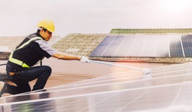 Side view Asian technicians cleaning blue outdoor solar photovoltaic panels to optimize functionality : Cleaning and inspection of solar panels on the roof of industrial plants : Selective focus clipart