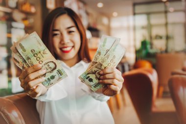 Mutluluk. Bir kafede oturan güzel bir kadın, günlük para harcamalarının mutluluğuyla birlikte 5000 baht Thai banknotunu gösteriyor: Seçici Odaklanma 