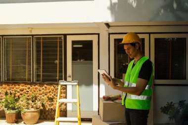 Projeden erkek mimar sorumlu, evin önündeki yenileme planı üzerinde çalışıyor, tamir listesini yazıyor, evi yeniliyor ve iş için hazırlanıyor..