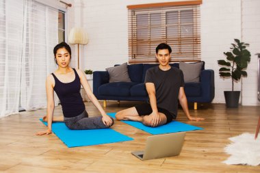 Ev kavramındaki yoga: Yakışıklı ve güzel Asyalı çift laptoplarında meditasyon yapıyor ve yoga yapıyor, oturma odasındaki yoga minderinde akıllarını dinlendiriyor..
