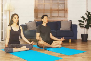 Evde yoga: çift meditasyon ve yoga yapıyor, akıllarını nilüfer ile sakinleştiriyor oturma odasındaki yoga minderinde poz veriyorlar..