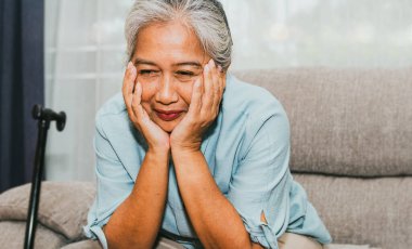 Sağlıklı bir portre, 60 yaşındaki Asyalı kadın neşeli, neşeli ve hayalperest bir şekilde oturdu, güzel anıları düşünerek, sakin bir hayat yaşayarak, evinde koltukta oturarak, mutlu, yaşlı kadın konsepti