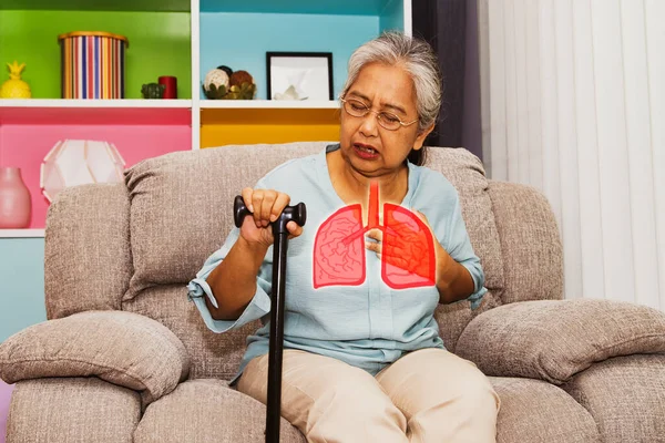 Yaşlı Asyalı kadın solunum zatürreesinden muzdarip: Kanepede oturan yaşlı kadın hasta, gripten hasta, depresyon, hızlı nefes alma ve göğüs ağrısı belirtileri gösteriyor.