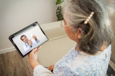 Üst düzey yaşlı kadın, evdeyken bir tıp uzmanıyla video görüşmesi yapıyor: dijital tablet üzerinde danışman bir doktorla görüntülü görüşme. Hasta yaşlı kadın online danışmanlık yapıyor..