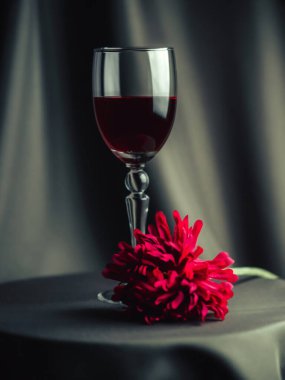 Masanın üzerinde bir bardak kırmızı şarap var. Yakınlarda kırmızı bir çiçek var. Sanatsal bulanıklık.