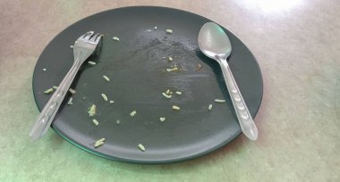 Üzerinde çatal ve kaşık olan siyah bir tabakta pirinç kırıntıları vardı..